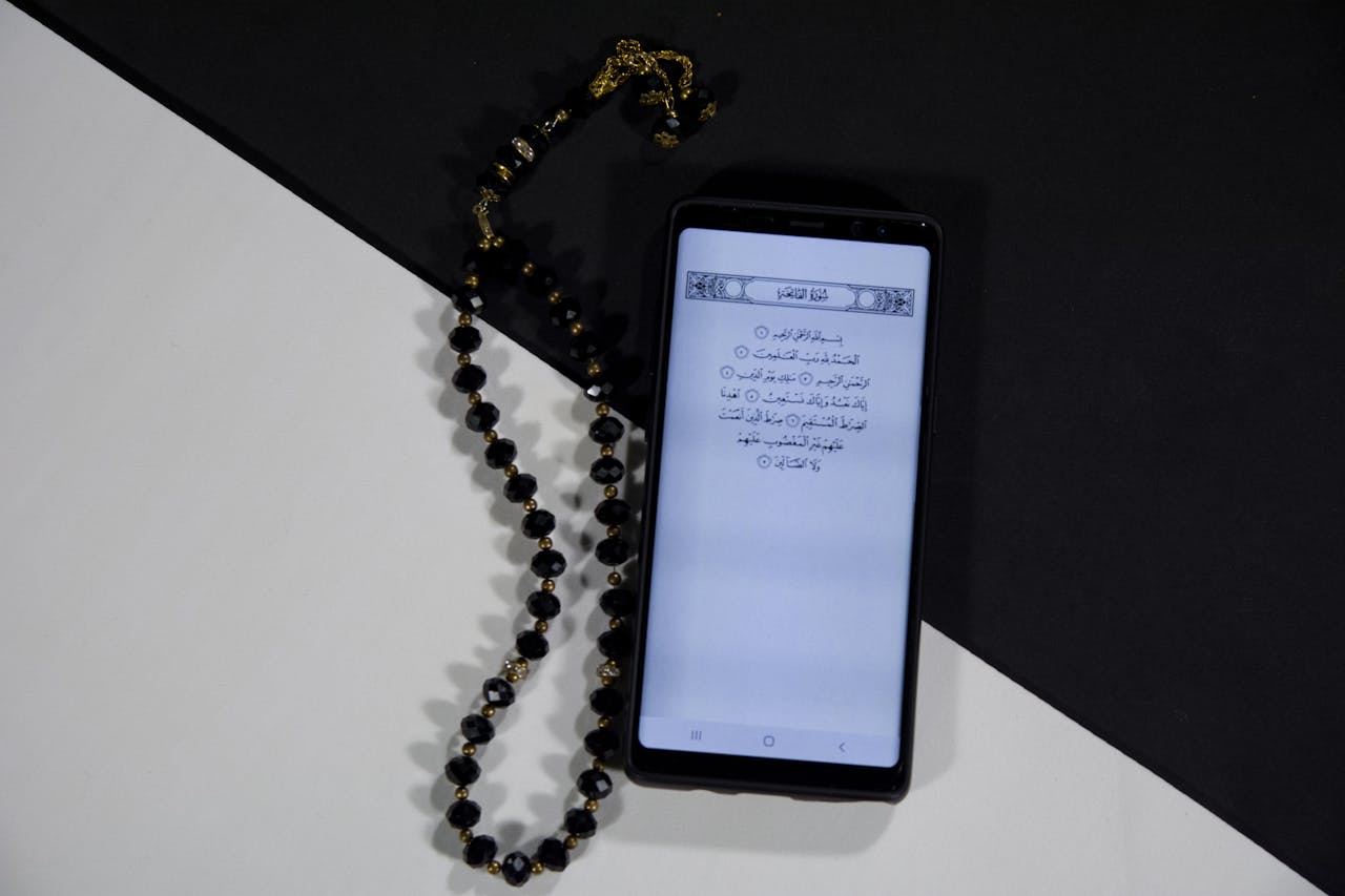 Smartphone showing Quran text with prayer beads on a black and white background.